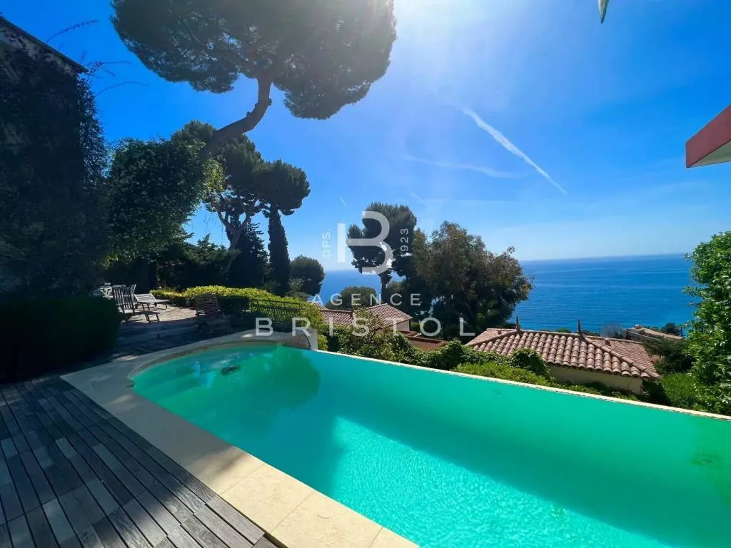 Piscine à débordement dans un jardin méditerranéen, avec pin parasol et vue sur la mer et la presqu’île